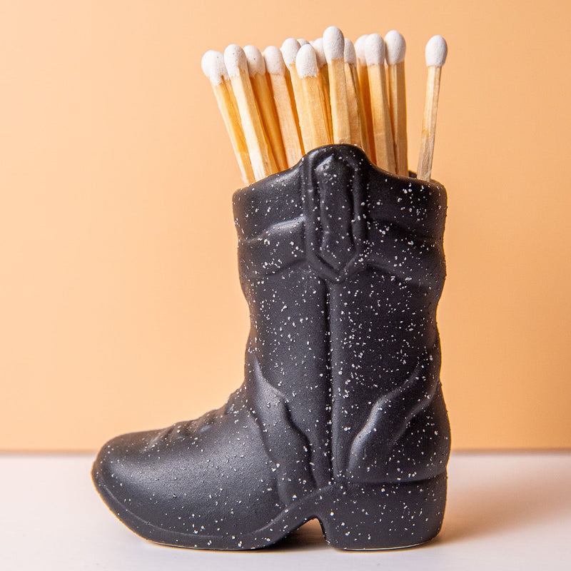Black cowboy boot-shaped matchbox with matches on a beige background