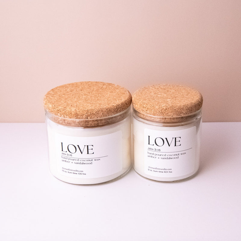 Two candles with cork lids labeled 'LOVE' on a light pink background